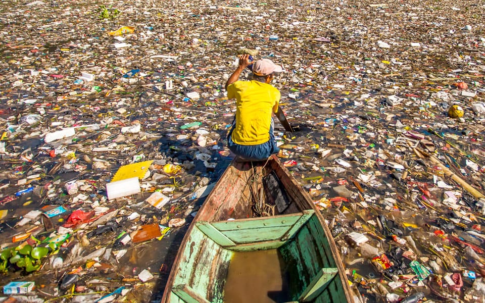 man paddling boat on water choked with rubbish